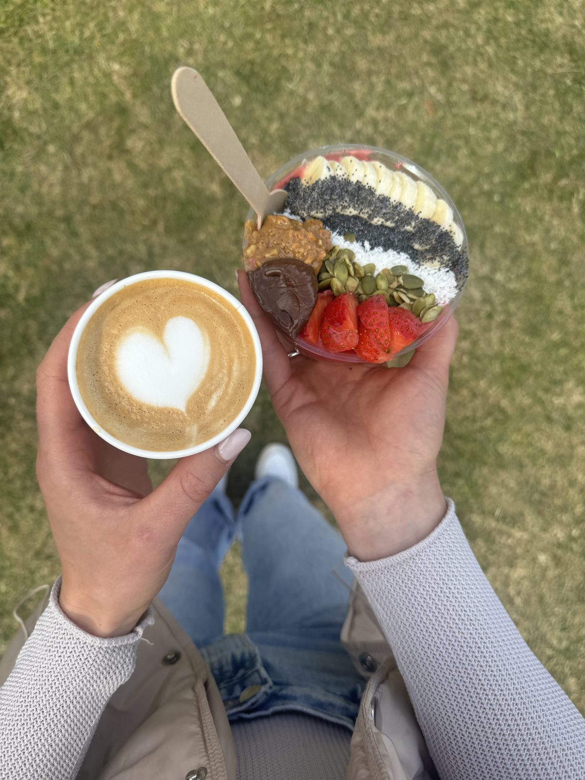 A latte and an açaí bowl held up outdoors